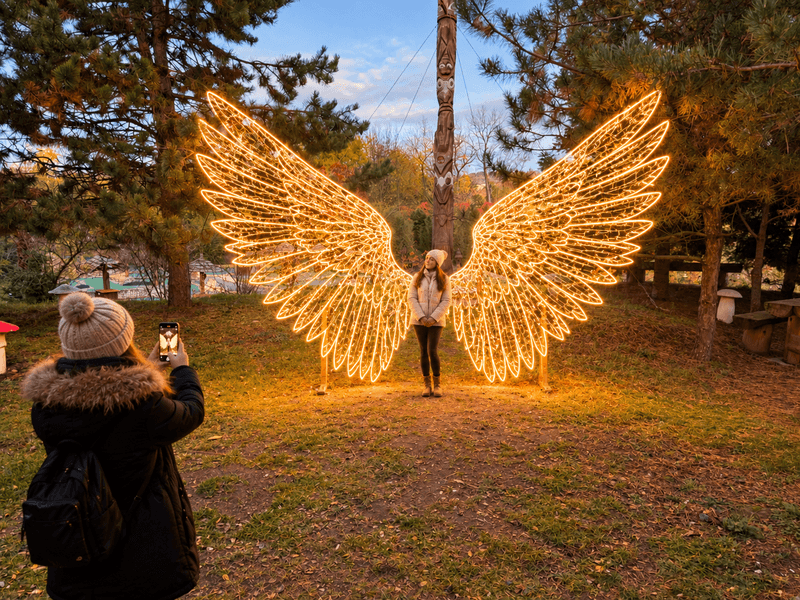 Svítící andělská křídla jako fotopoint, dívka se před nimi fotí